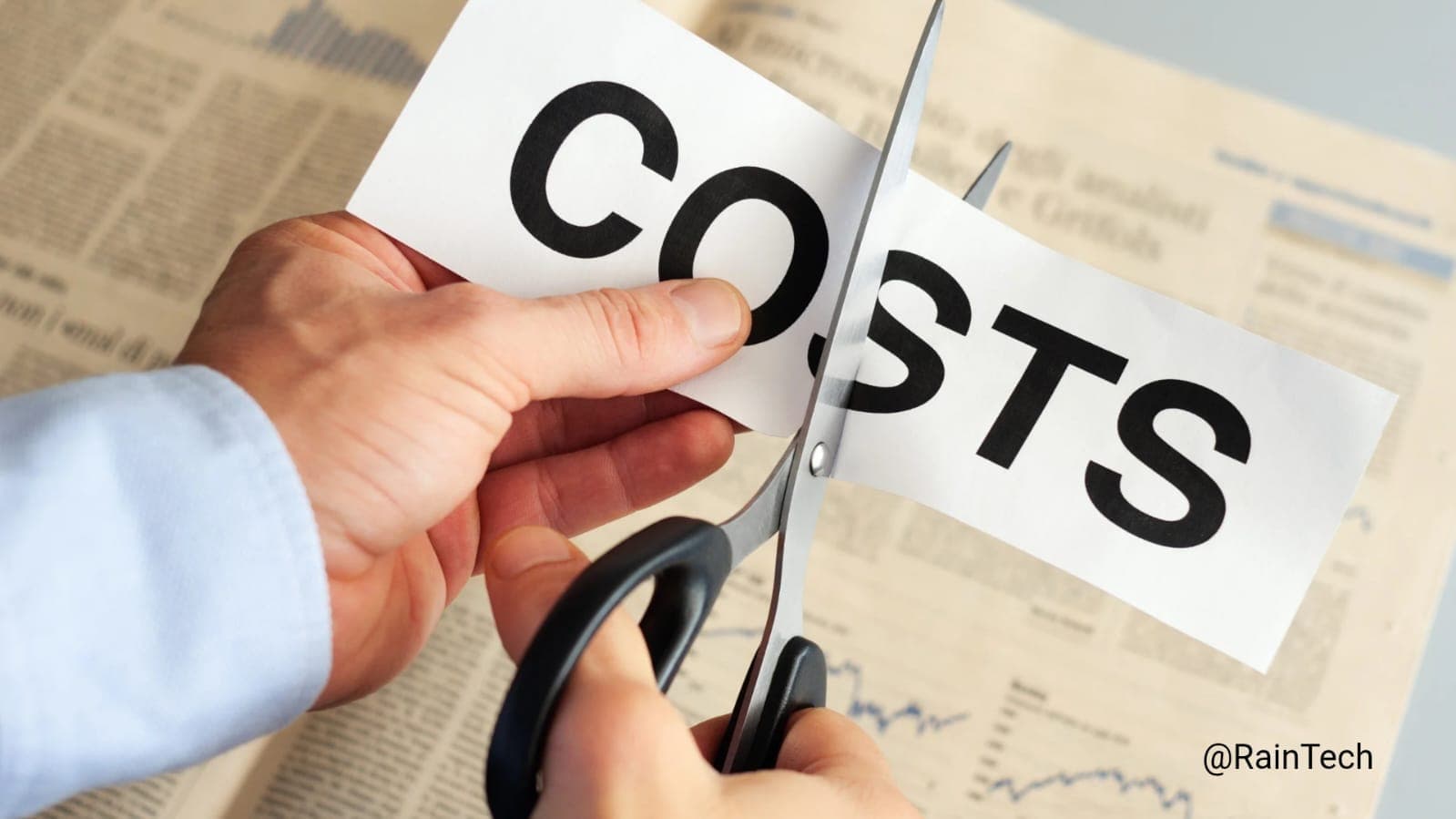 Hand cutting a paper with the word COSTS using scissors, symbolizing cost reduction and savings. 