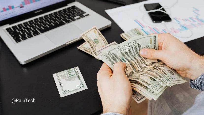 Person counting US dollar bills in front of a laptop, representing the massive $113k cost savings for startups hiring engineers through RainTech EOR.