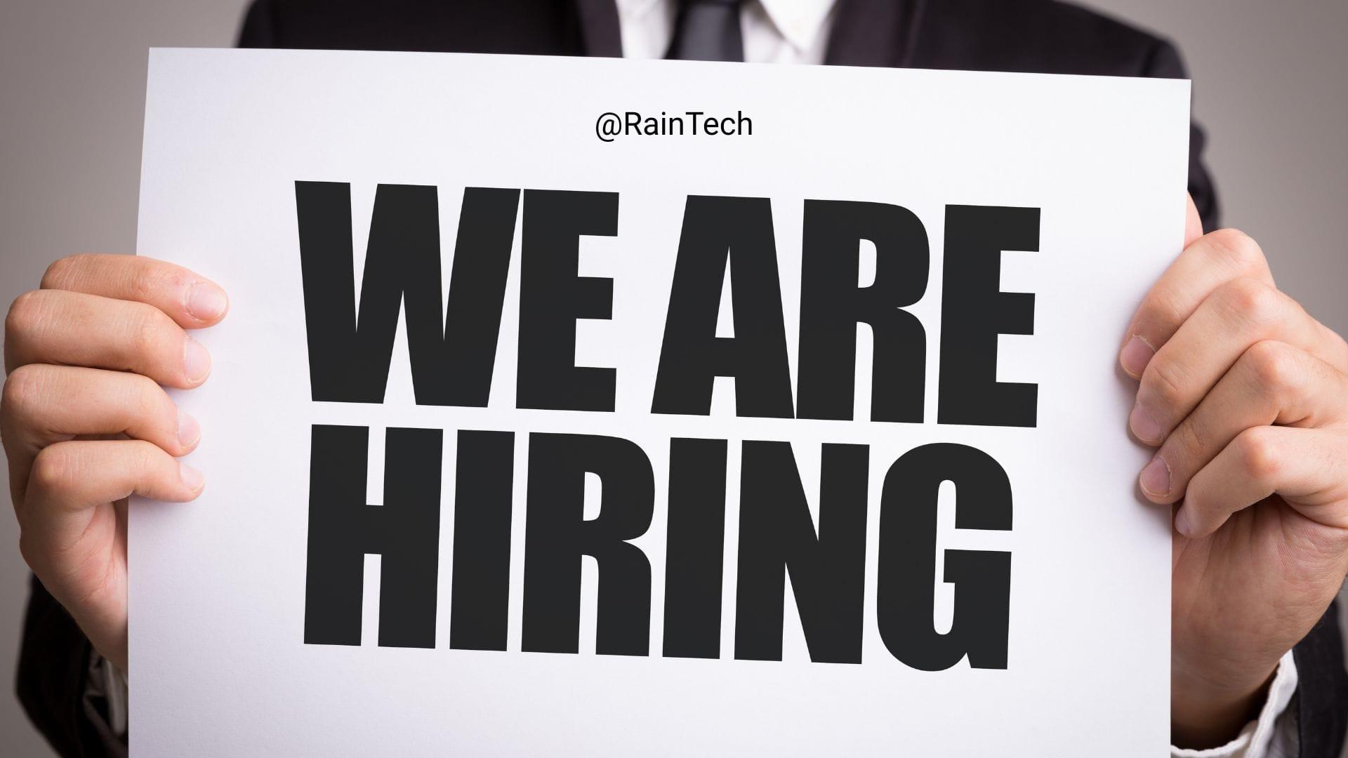 A professional holding a 'We Are Hiring' sign for RainTech, representing a remote .NET Backend Engineer job opportunity.