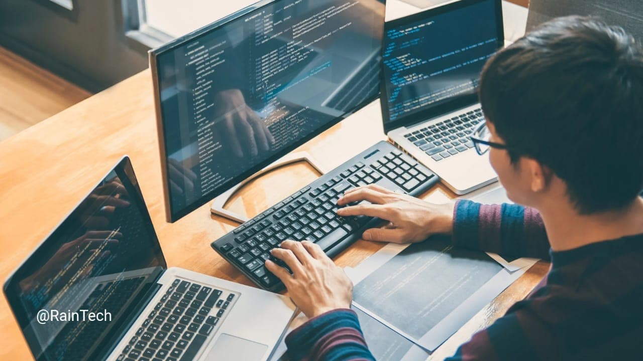 Professional Indonesian software developer coding with multiple laptops and screens.