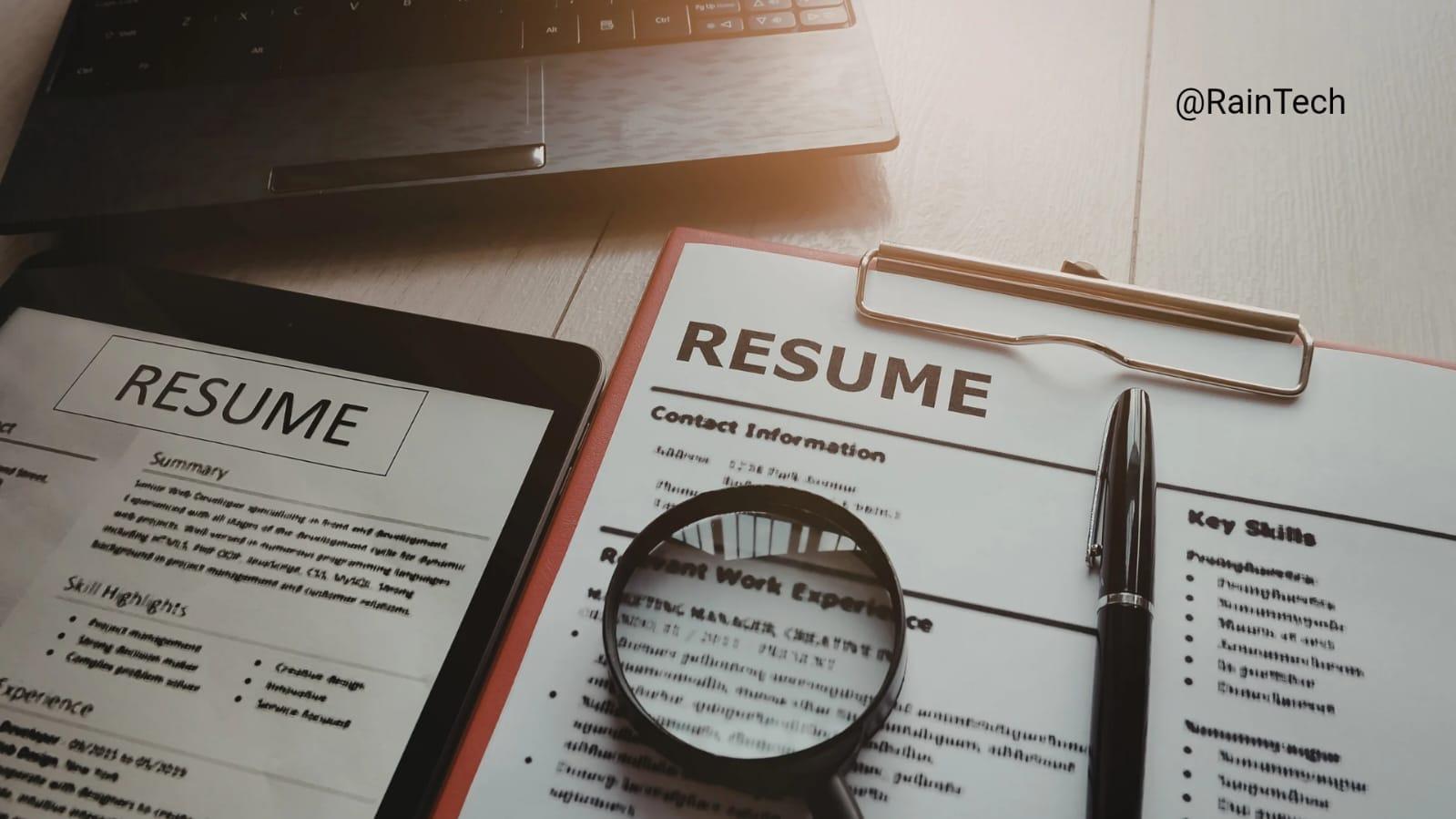 A magnifying glass over a resume next to a laptop, representing the process of hiring remote engineers in Indonesia, Vietnam, and the Philippines.