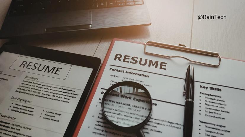 A magnifying glass over a resume next to a laptop, representing the process of hiring remote engineers in Indonesia, Vietnam, and the Philippines.